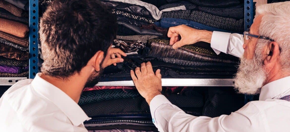 Two men inspecting fabric samples in a textile warehouse.